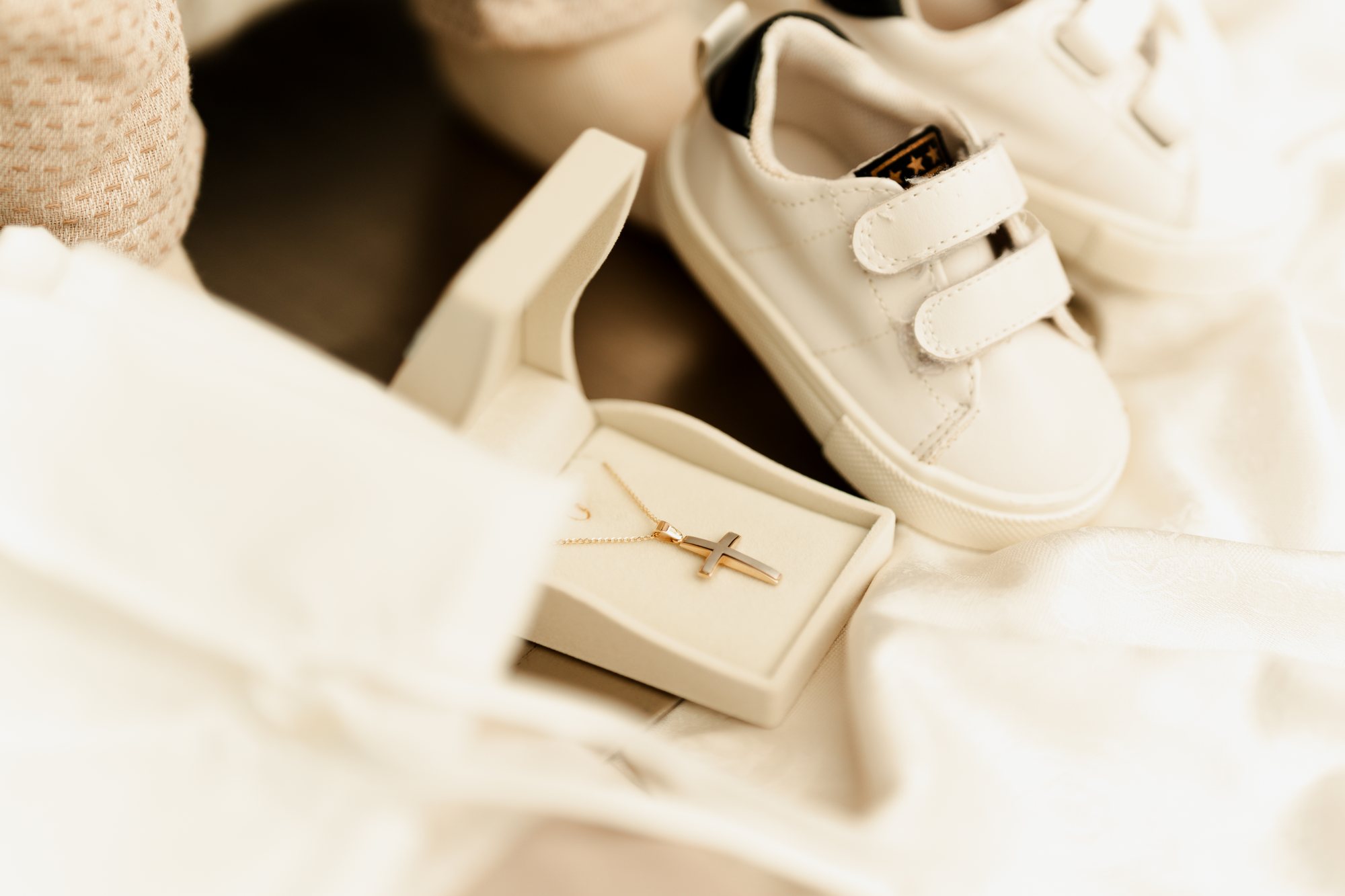 Baby shoes and a gold cross in a gift box on white linen