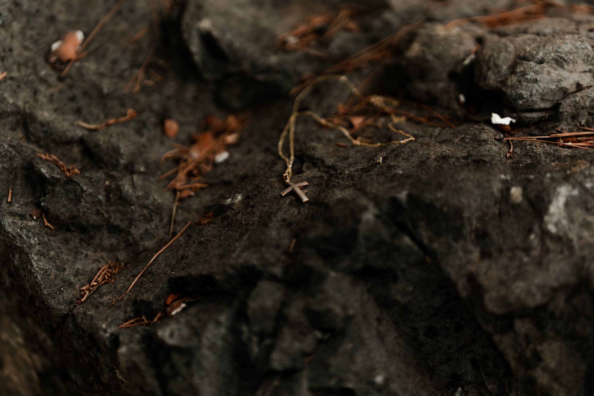 A gold cross and chain lying on dark volcanic stone