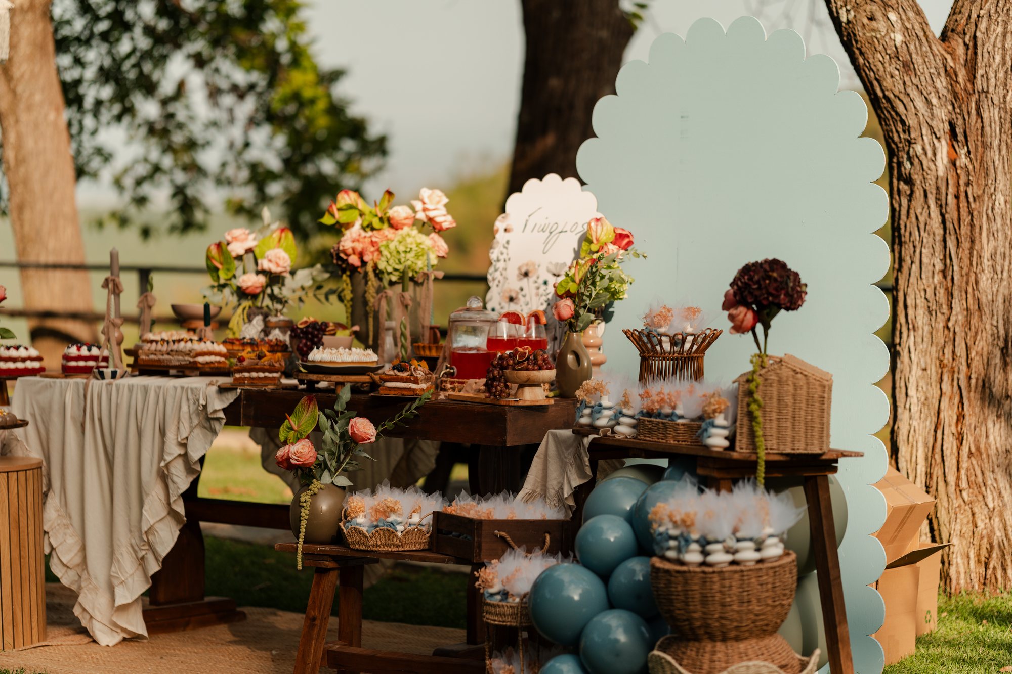 The reception table under the trees with flowers and blue balloons