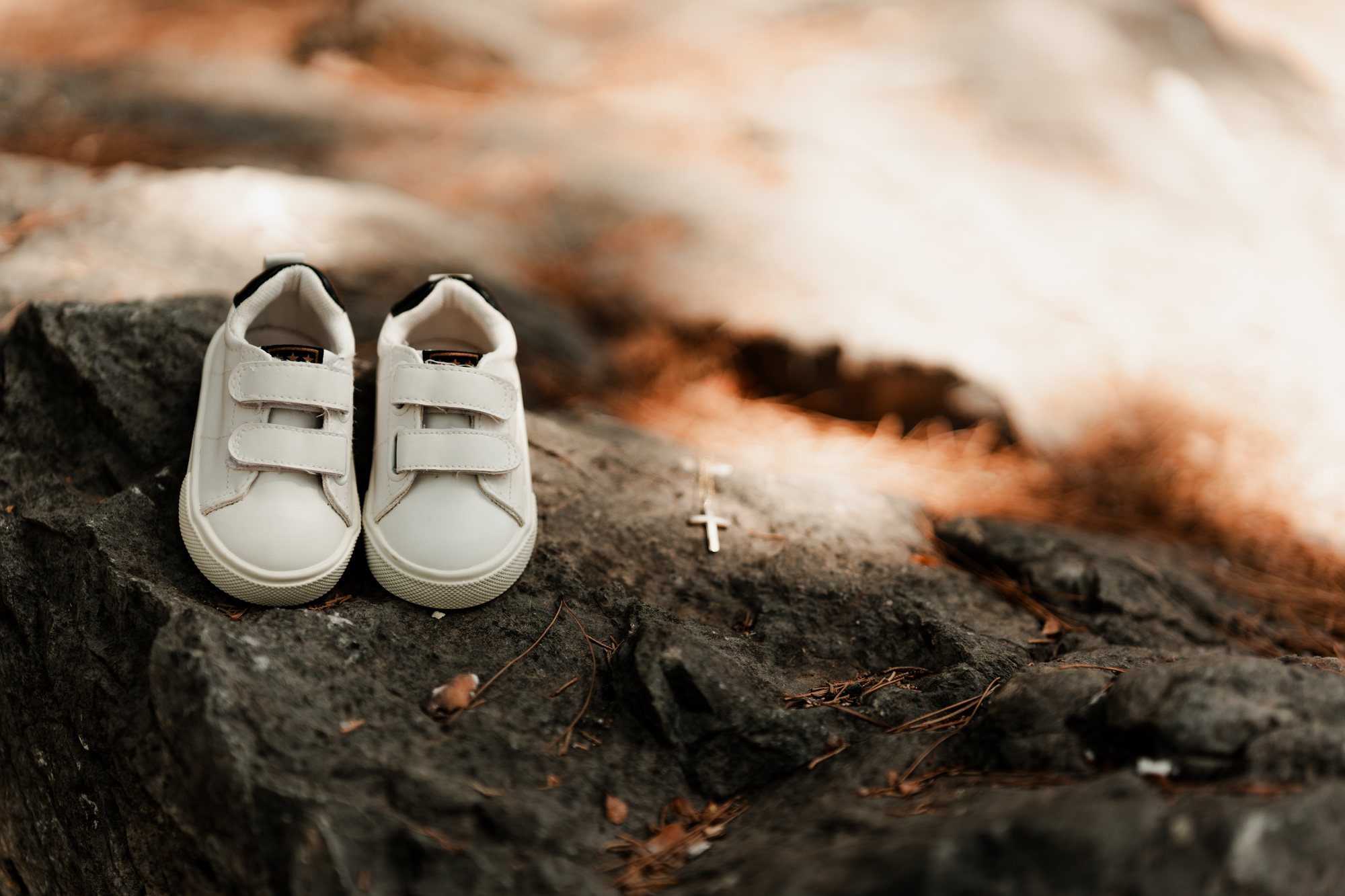 White baby shoes and a gold cross on a rock in dappled light