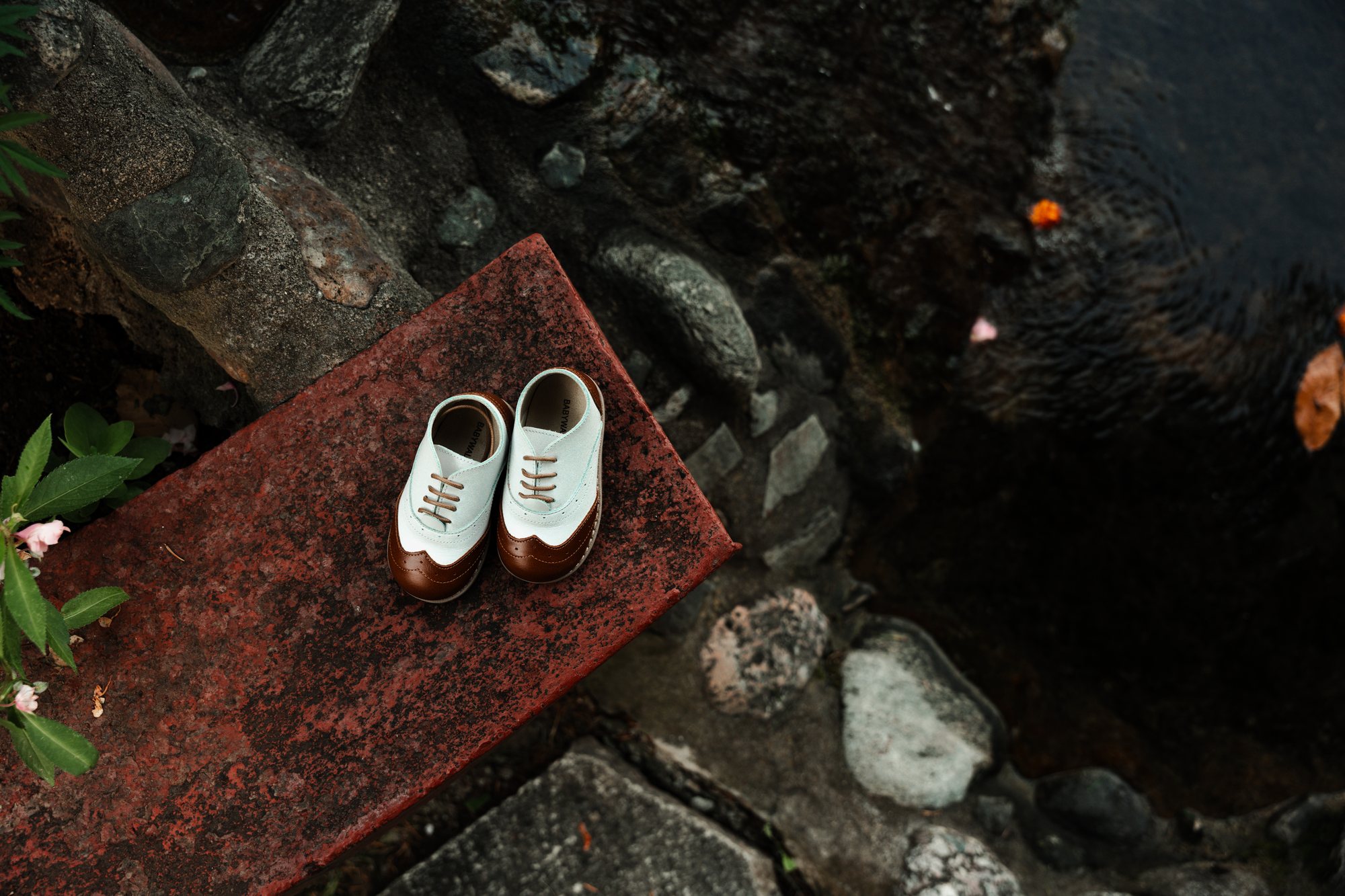 White baby shoes on a red tray set on river stones