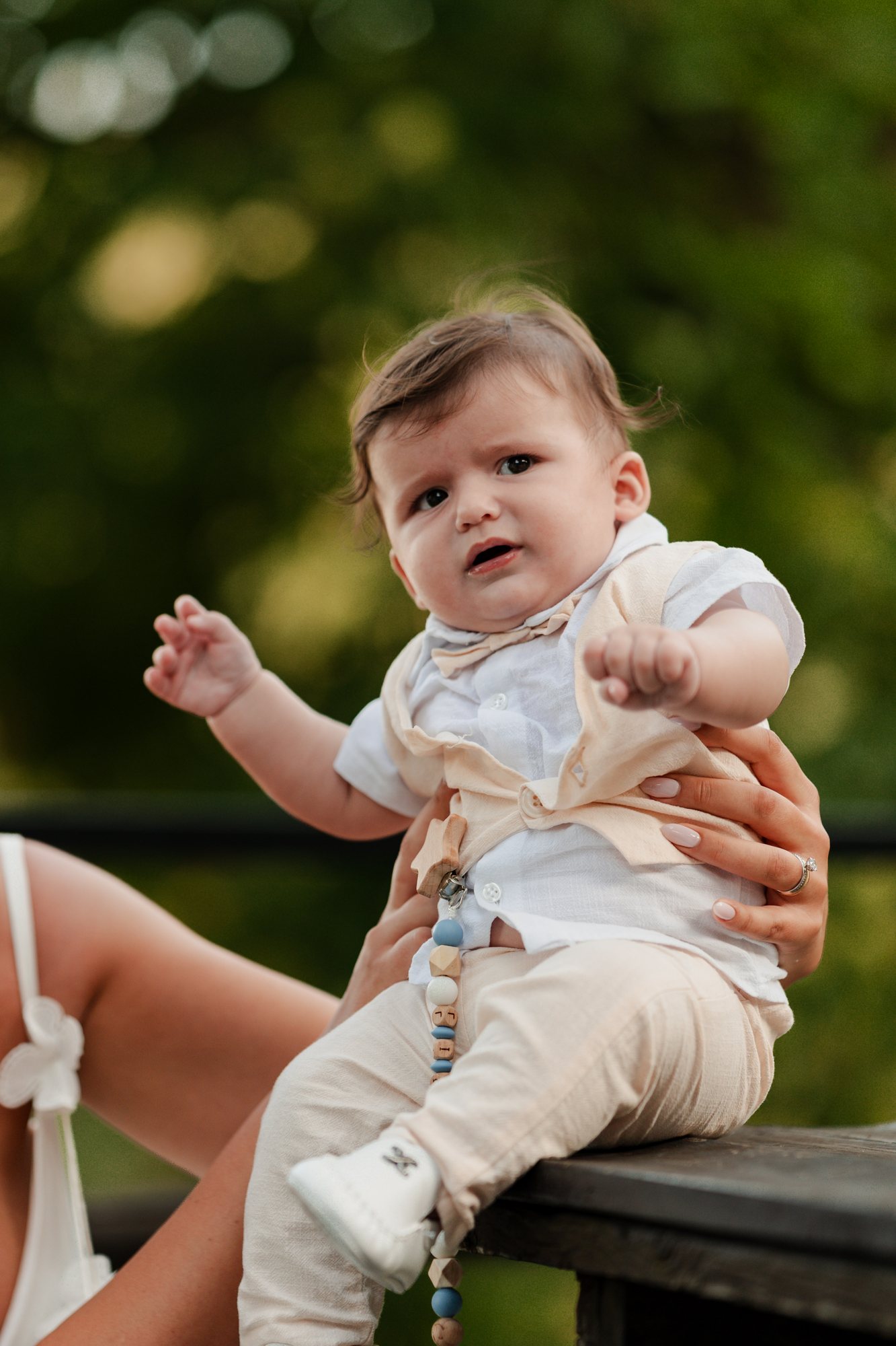 The baby in his christening outfit sitting on a bench in the garden