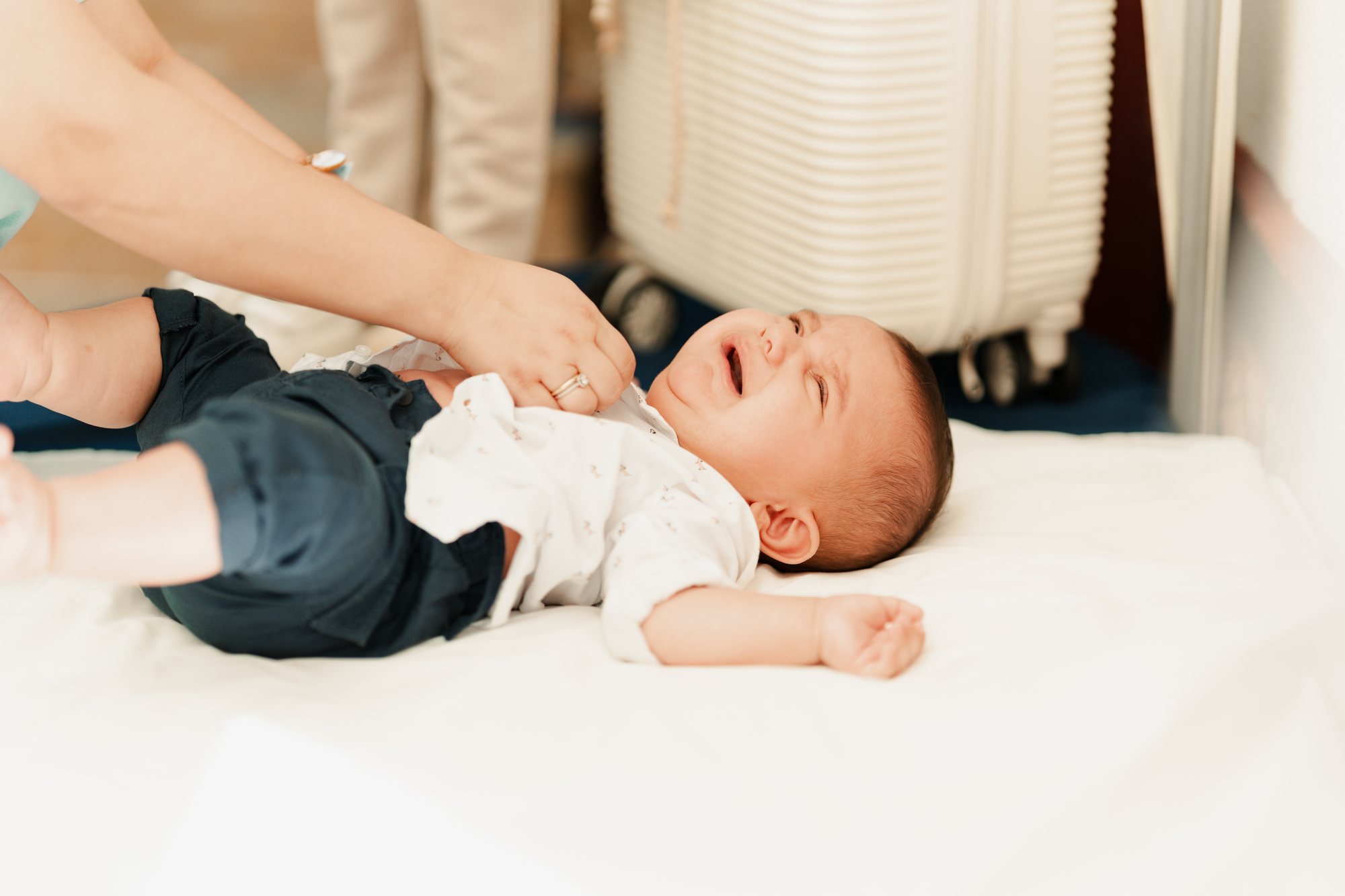 A baby laughing on a white blanket as his parents undress him