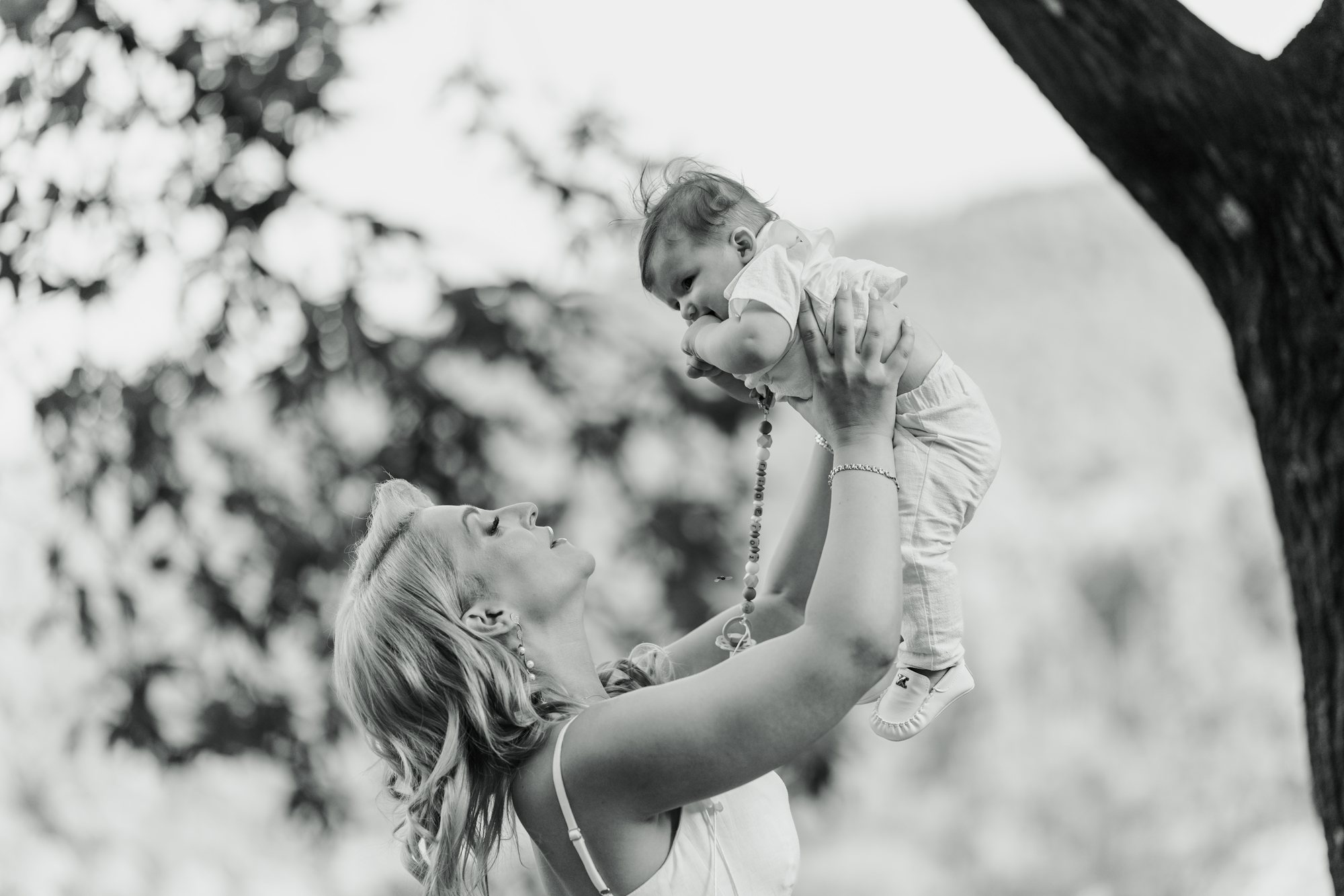 Black and white photo of a mother lifting her baby under a tree