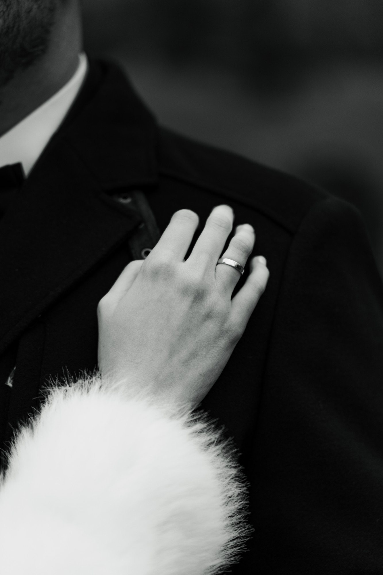 The bride’s hand with her wedding ring resting on the groom’s dark coat