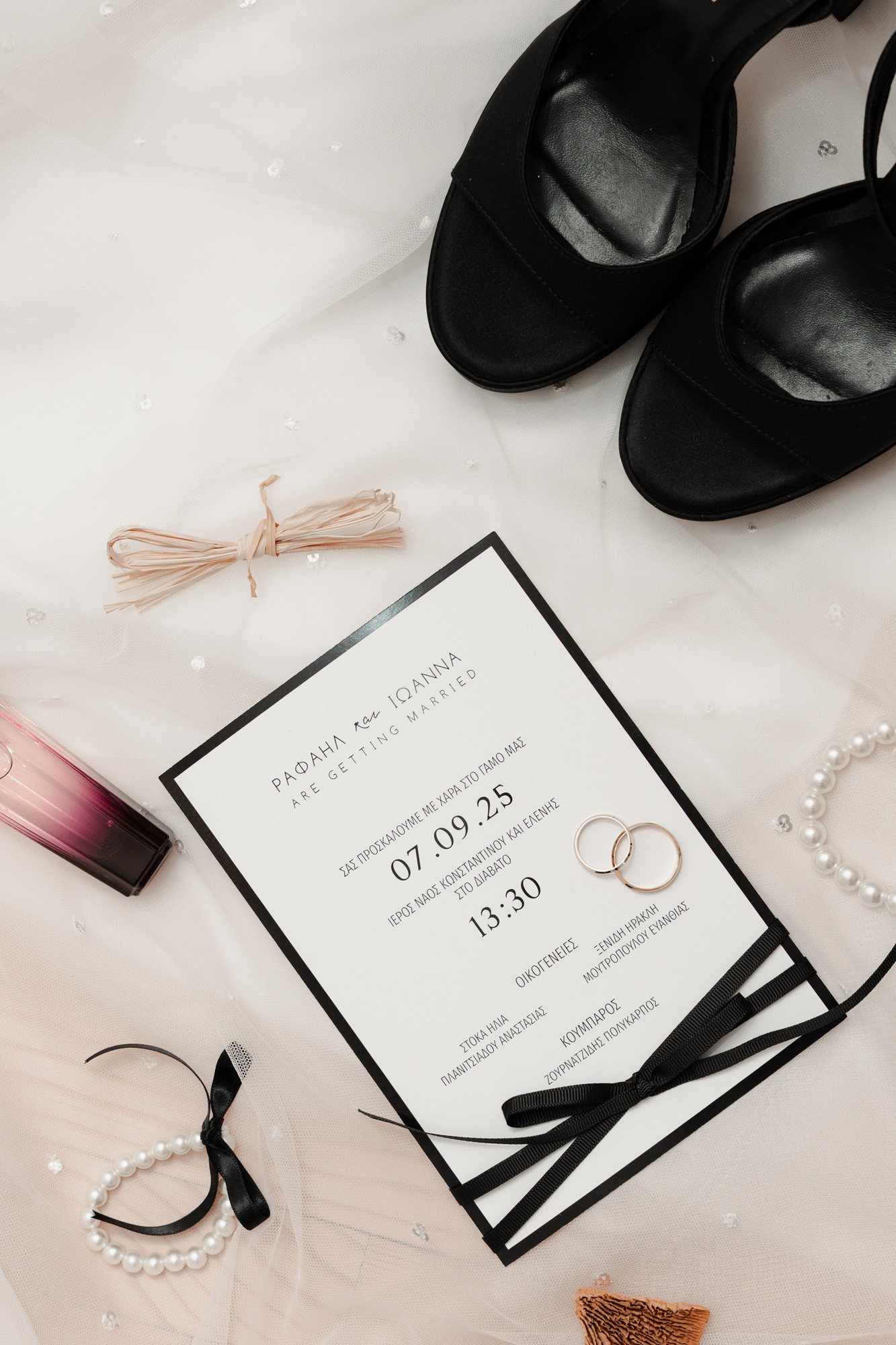 Wedding invitation dated 07.09.25 laid out with black heels, pearls and a ribbon