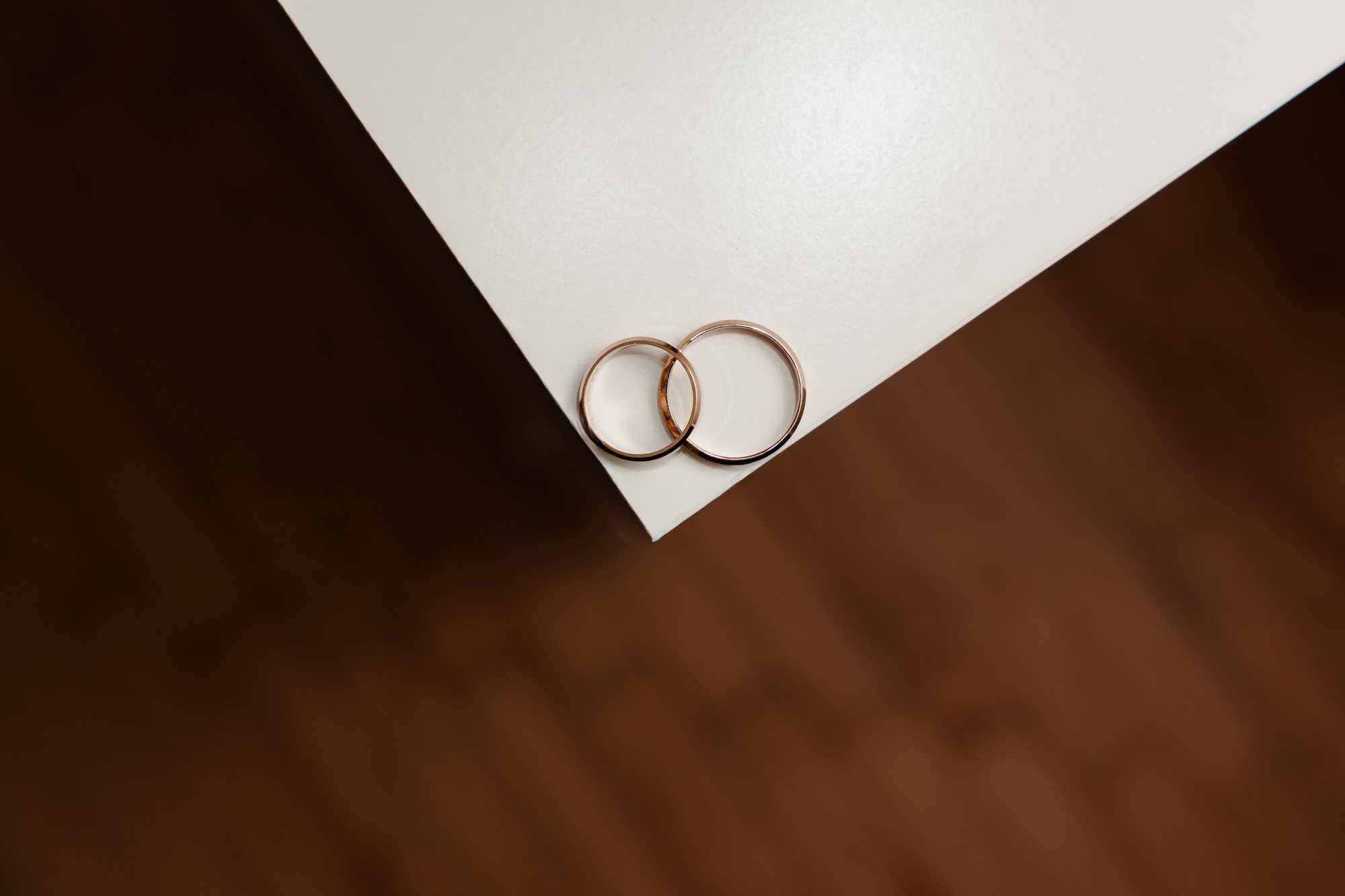 Two gold rings resting on the corner of a white card over a dark wooden table