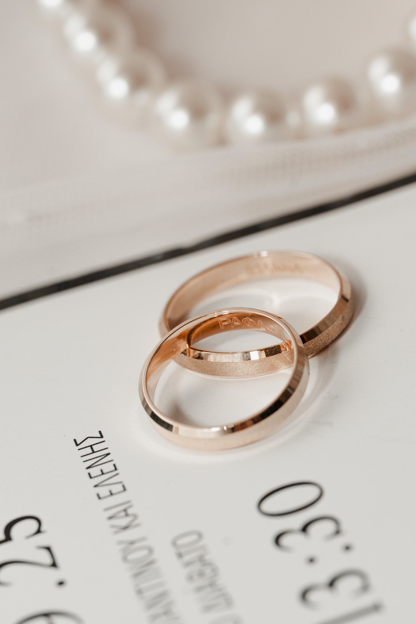 Two gold wedding rings on the invitation beside a string of pearls