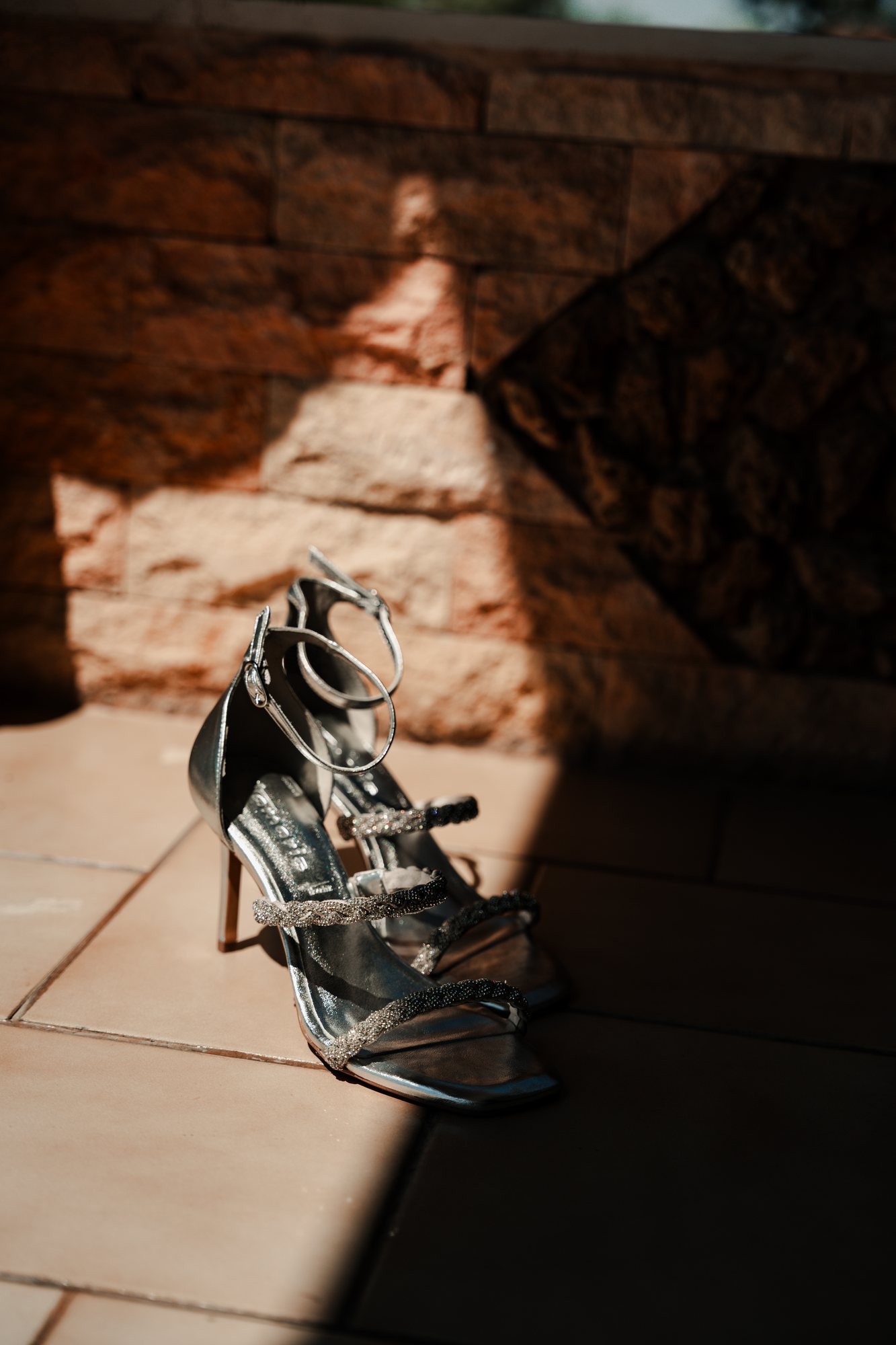 Silver strappy sandals on a tiled floor in a patch of afternoon sun
