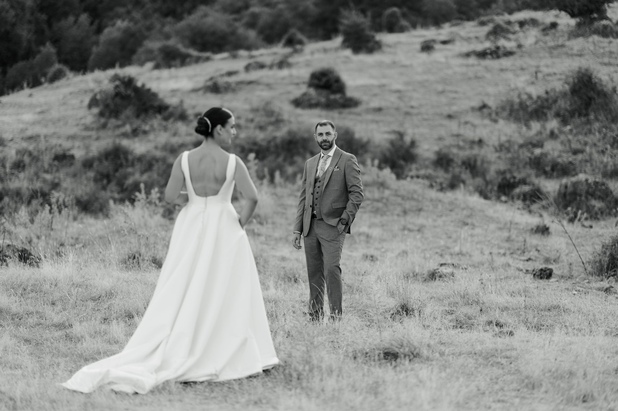 Bride and groom stand a few steps apart on a hillside