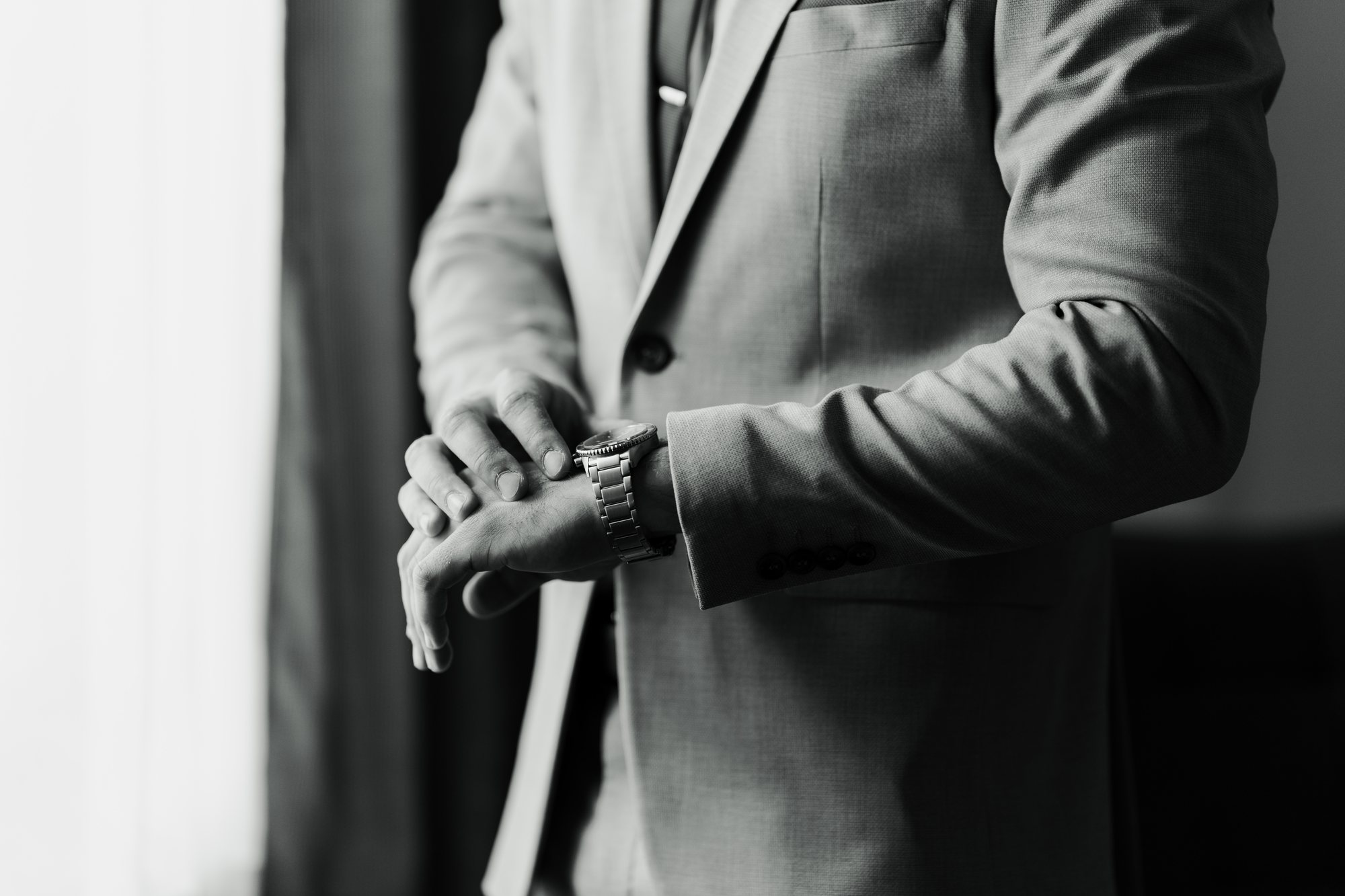 Black and white close-up of the groom’s folded hands and watch