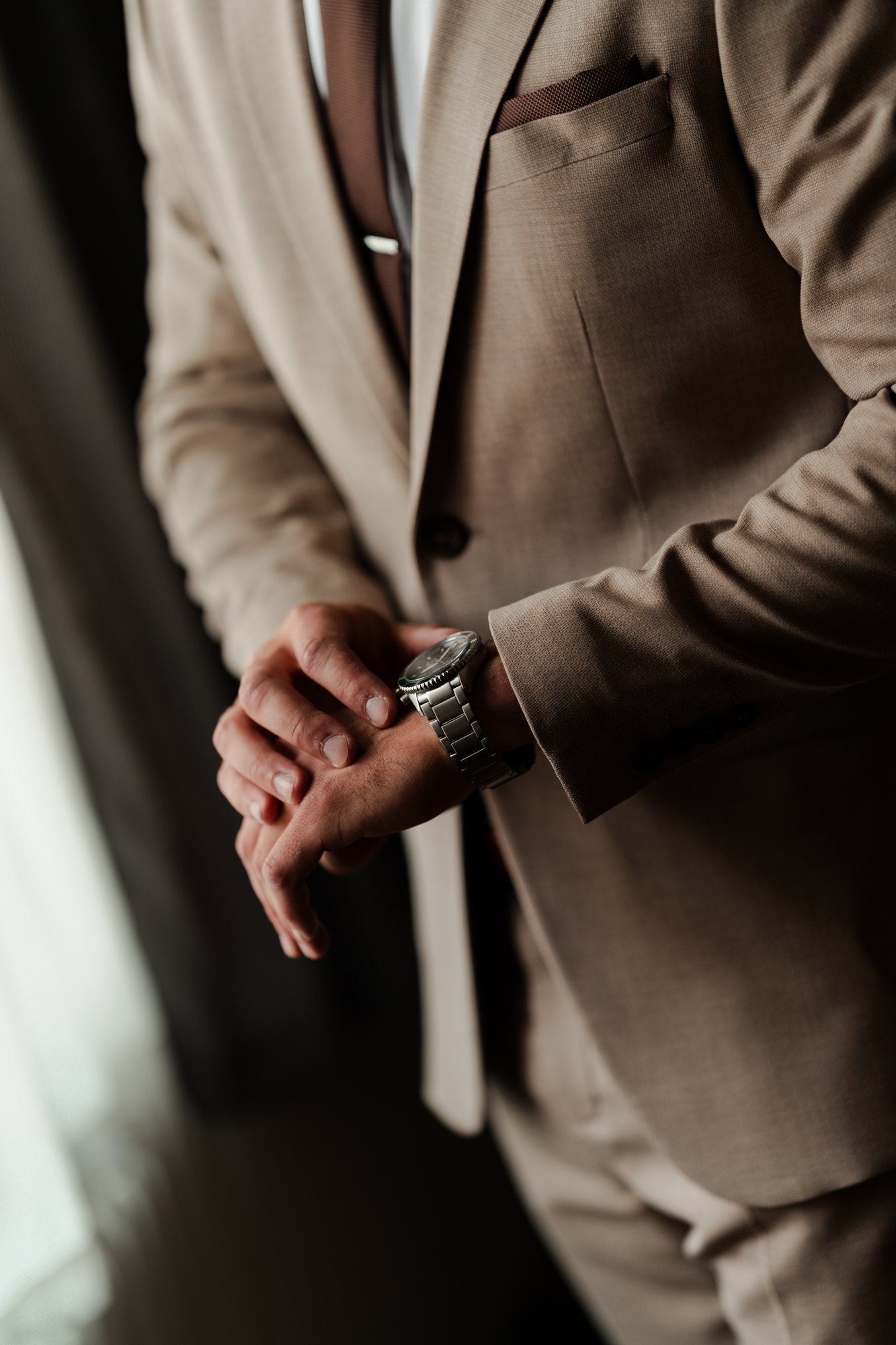 Close-up of the groom’s hands and watch against his beige suit