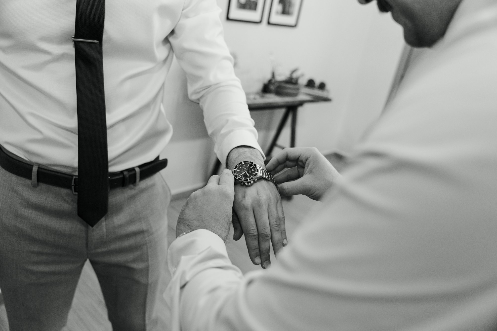 Black and white close-up of hands fastening the groom’s cuff