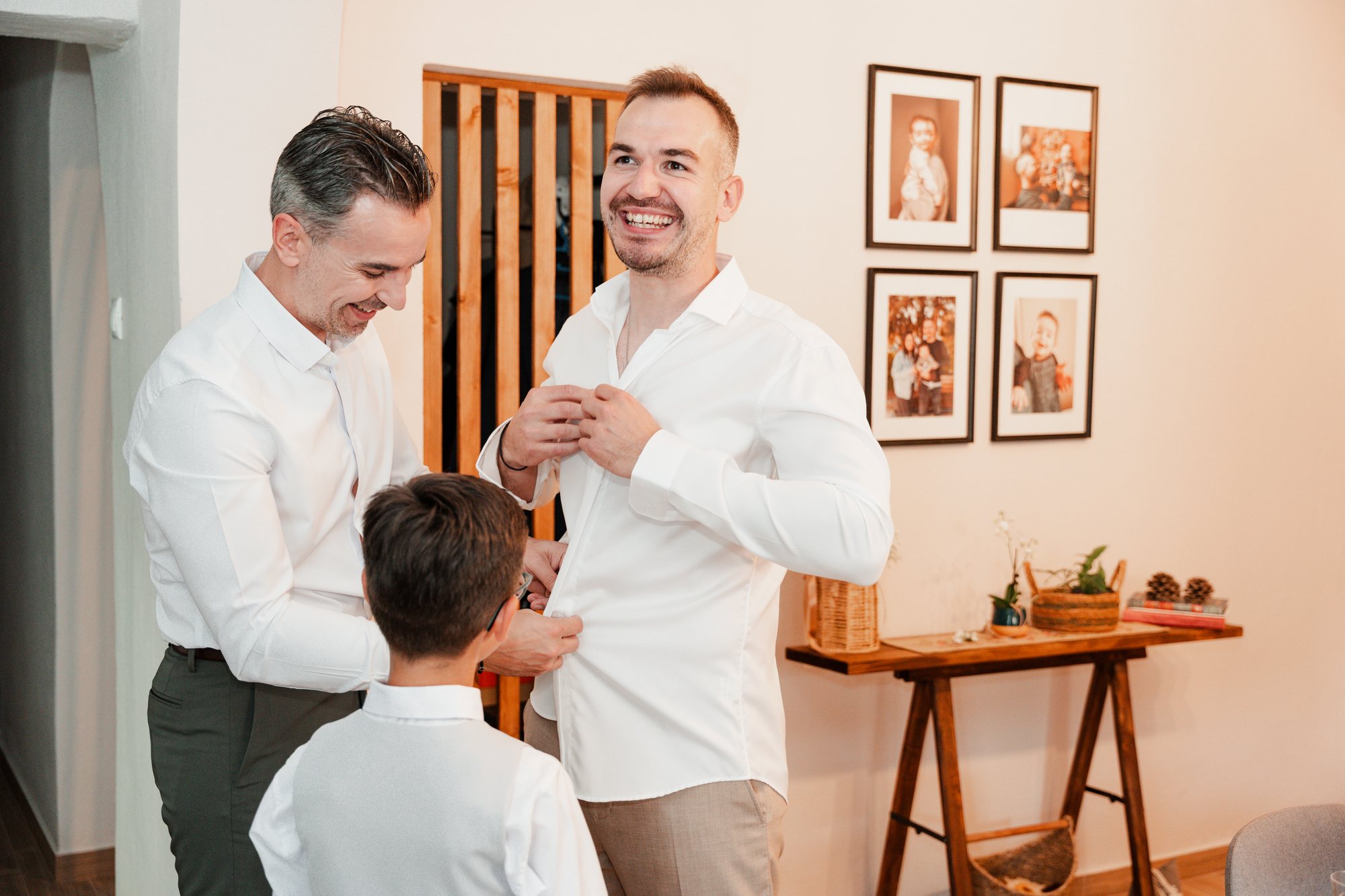 The groom buttons his shirt, helped by an older man and a young boy